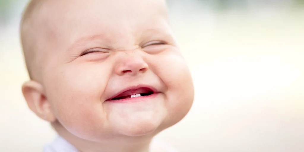 smiling baby with closed eyes and visible teeth, radiating joy against a soft, blurred background