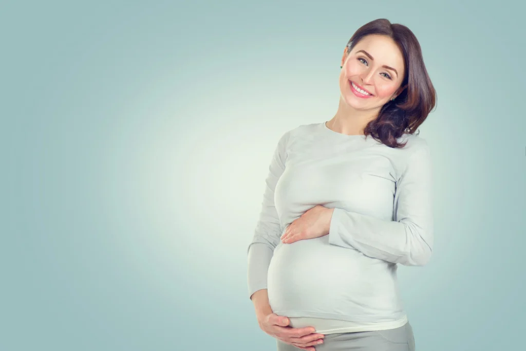 happy pregnant woman smiling and gently cradling her belly against a soft blue background